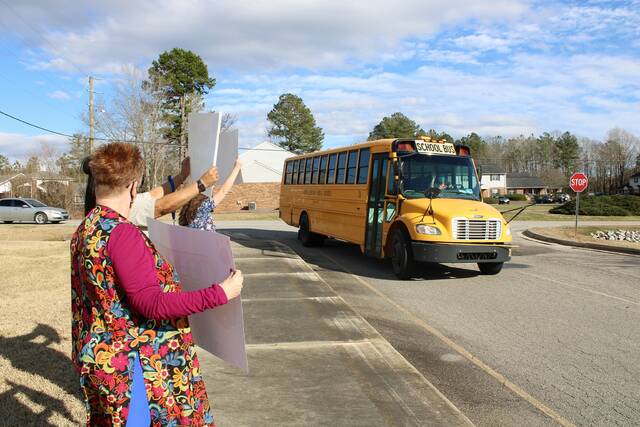 Community members hold signs in support of bus drivers as a bus passes by.
                                 Contributed photo